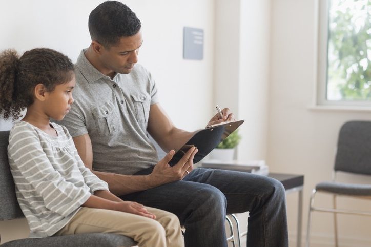 Father waiting alongside daughter while filling out paperwork